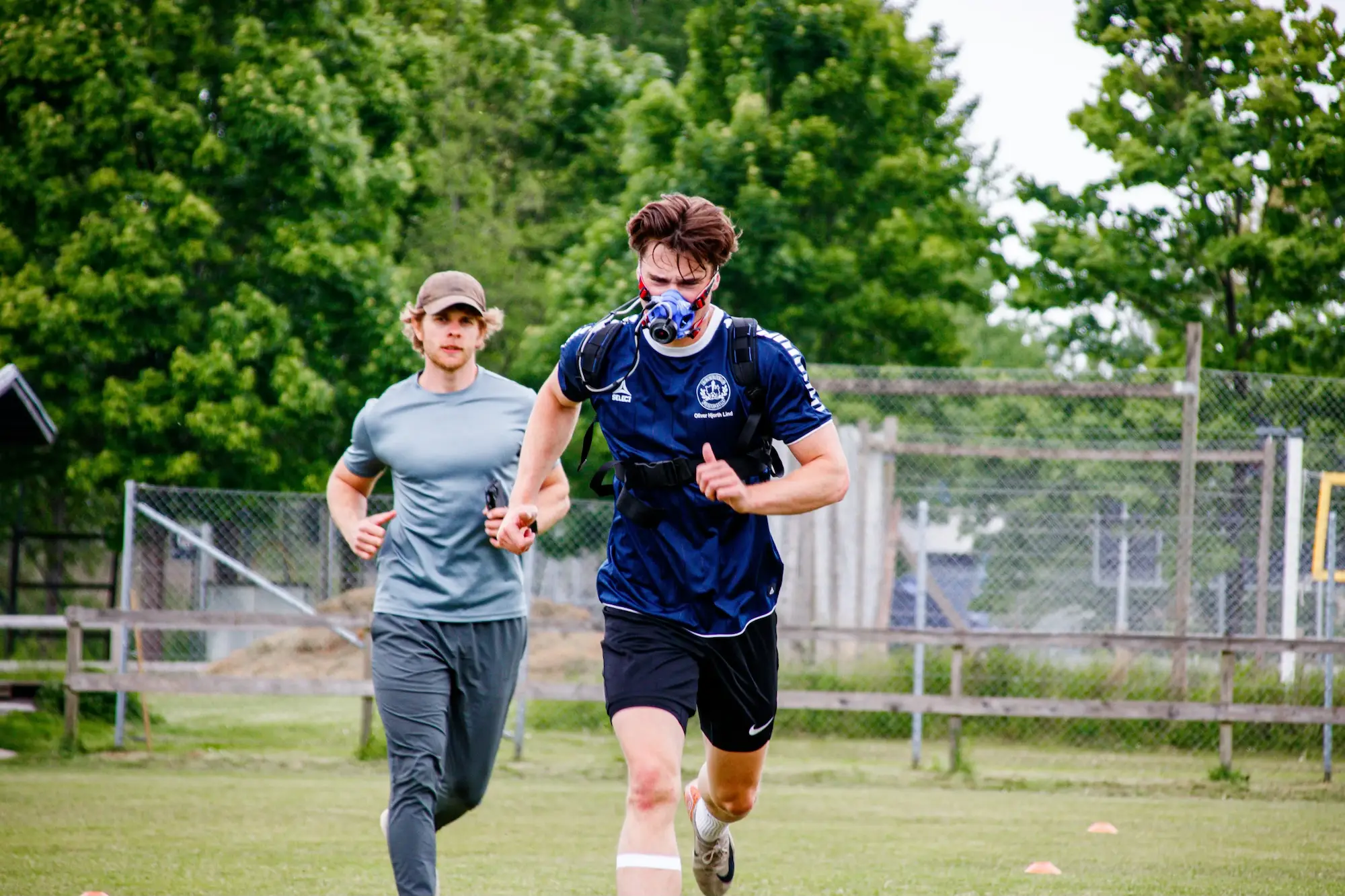 Athlete wearing a training mask running outdoors while being supervised by a coach